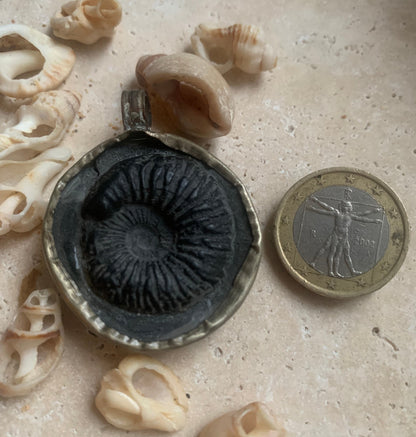 Fossilized ammonite from Nepal, measuring 45x35x12 millimeters. This authentic and unique piece reveals the natural spirals and fascinating patterns of this fossil. Comes with a drawstring, ready to wear or give as a gift!