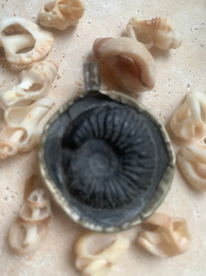 Fossilized ammonite from Nepal, measuring 45x35x12 millimeters. This authentic and unique piece reveals the natural spirals and fascinating patterns of this fossil. Comes with a drawstring, ready to wear or give as a gift!