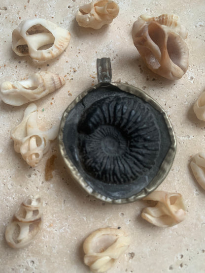 Fossilized ammonite from Nepal, measuring 45x35x12 millimeters. This authentic and unique piece reveals the natural spirals and fascinating patterns of this fossil. Comes with a drawstring, ready to wear or give as a gift!