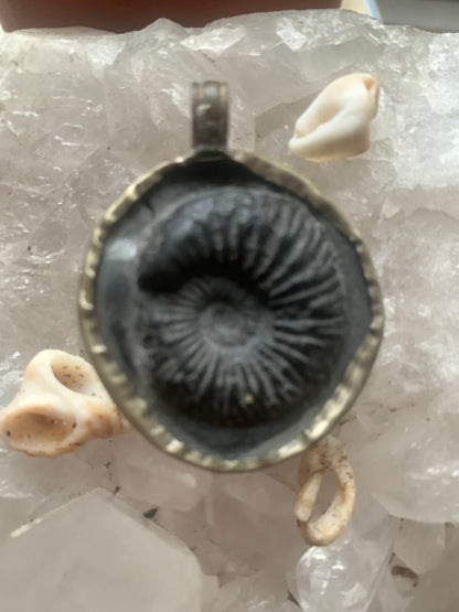 Fossilized ammonite from Nepal, measuring 45x35x12 millimeters. This authentic and unique piece reveals the natural spirals and fascinating patterns of this fossil. Comes with a drawstring, ready to wear or give as a gift!